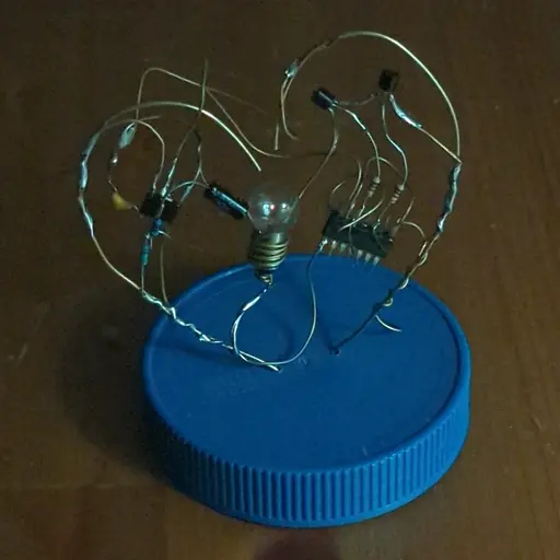 A fully-lit demonstration of the final sculpture. Brass wire shaped like a heart frames an incandescent lightbulb that pulses with the rhythm of a beating heart.
