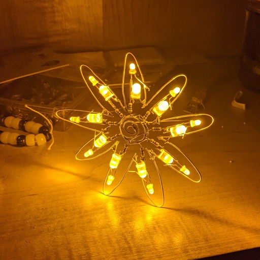An amber LED flower sitting on my messy bookshelf.